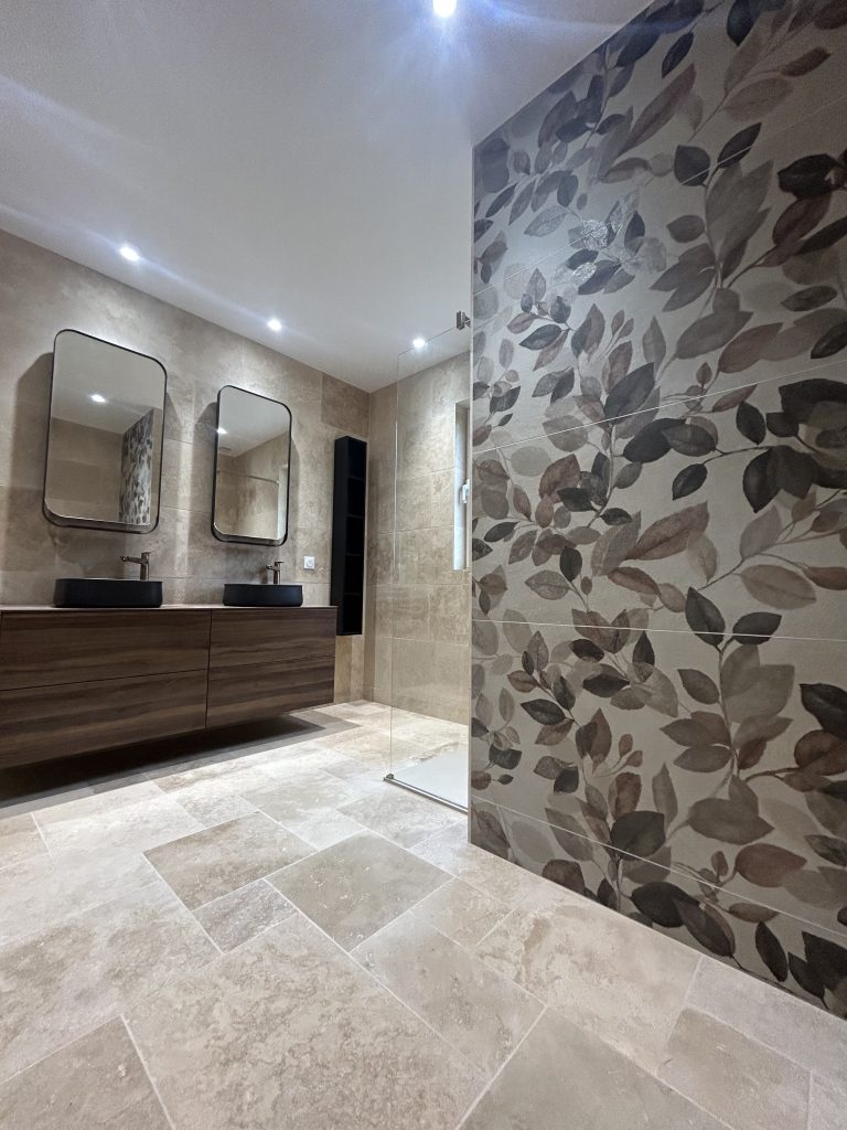 Vue d'ensemble d'une salle de bain rénovée avec travertin et meuble vasque en bois