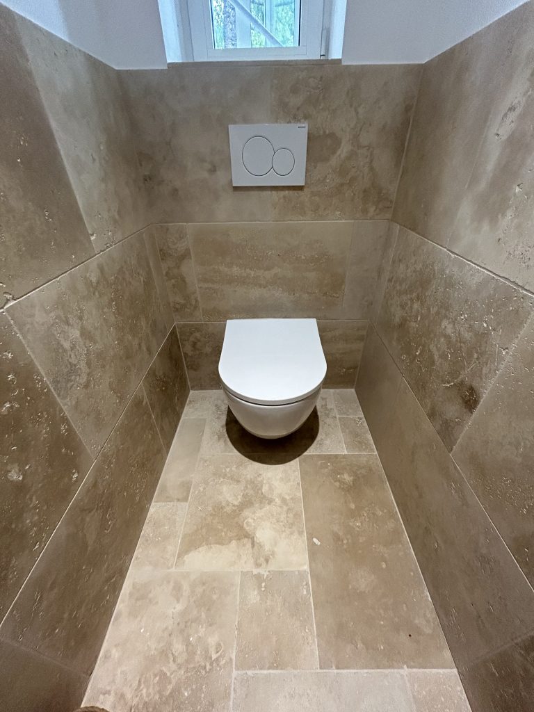 WC suspendu intégré dans une salle de bain rénovée avec carrelage effet travertin