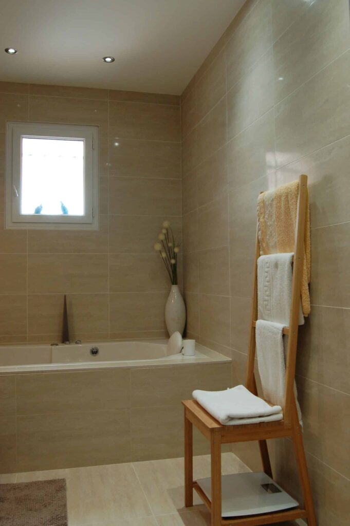 Carrelage mural beige et porte serviettes dans une salle de bain rénovée.