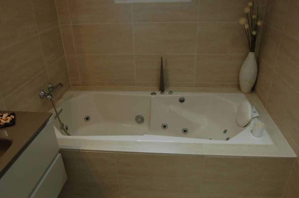 Baignoire balnéo blanche avec habillage en carrelage beige.
