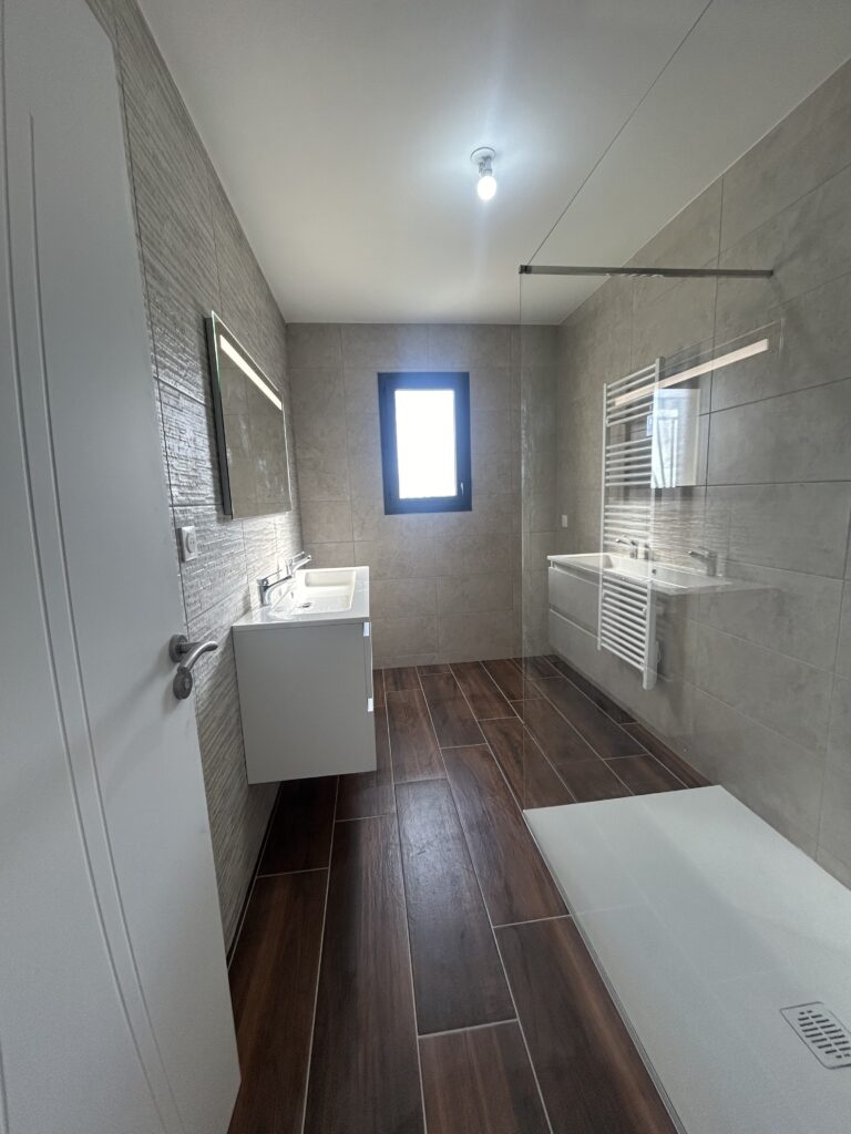 Salle de bain moderne rénovée avec douche à l'italienne, double vasque et carrelage effet bois.