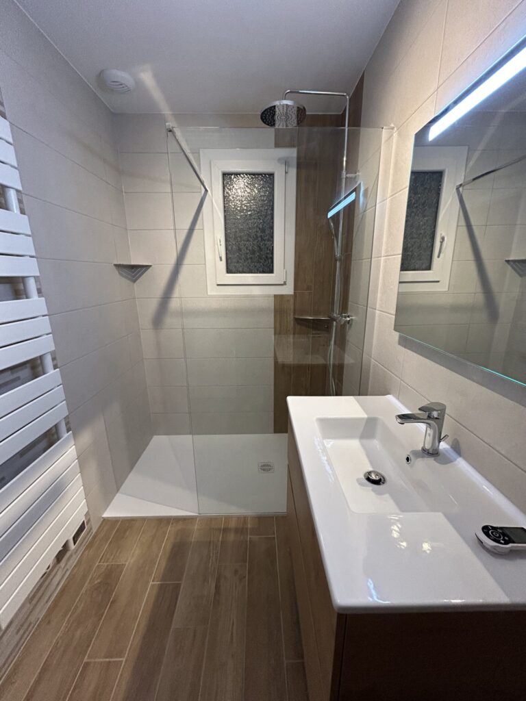 Salle de bain moderne avec meuble suspendu, miroir lumineux et revêtement imitation bois.
