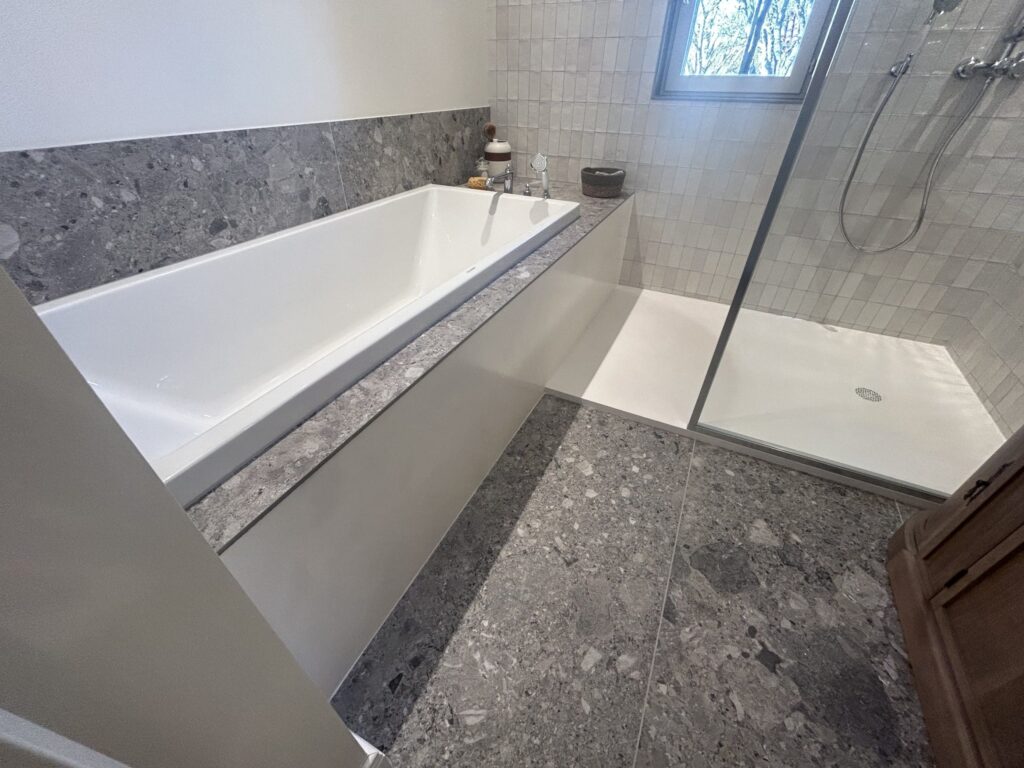 Sol effet terrazzo reliant la baignoire et la douche à l'italienne dans une salle de bain rénovée à Salette.