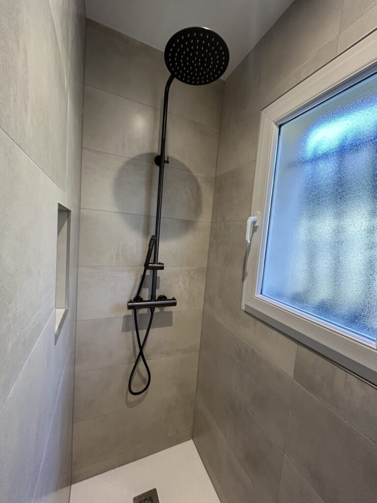 Douche à l'italienne avec robinetterie noire dans une salle de bain rénovée