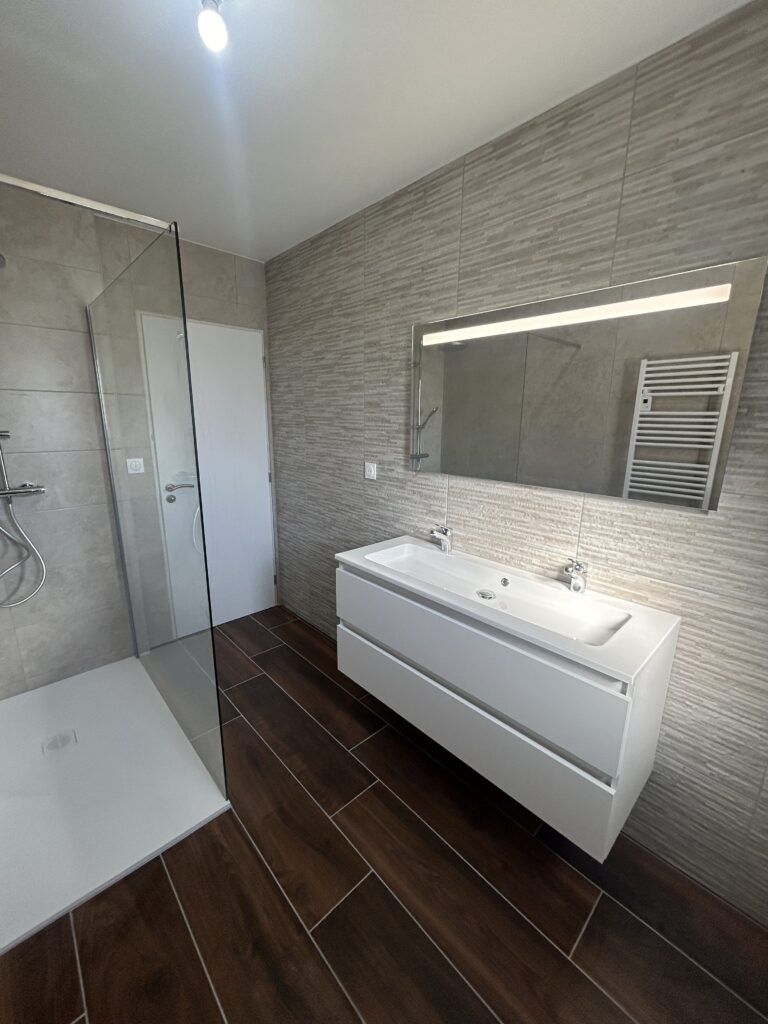 Salle de bain rénovée avec douche à l'italienne et meuble double vasque suspendu.